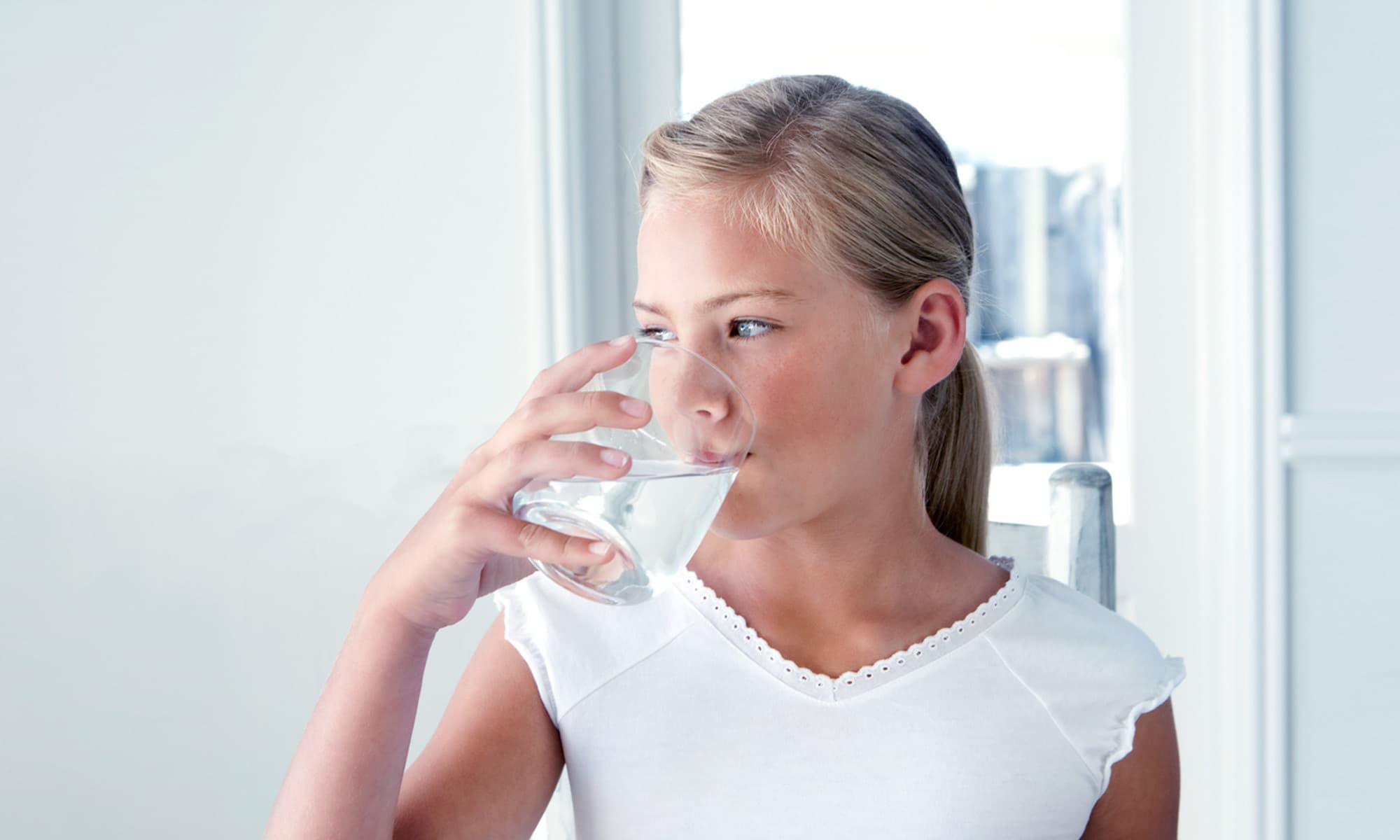A child drinking a glass of water at a kitchen table